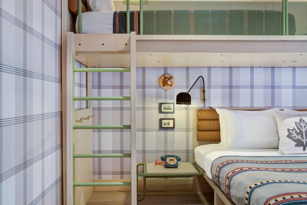 A bunk bed with a ladder, a bedside table with a telephone, and a wall-mounted lamp.