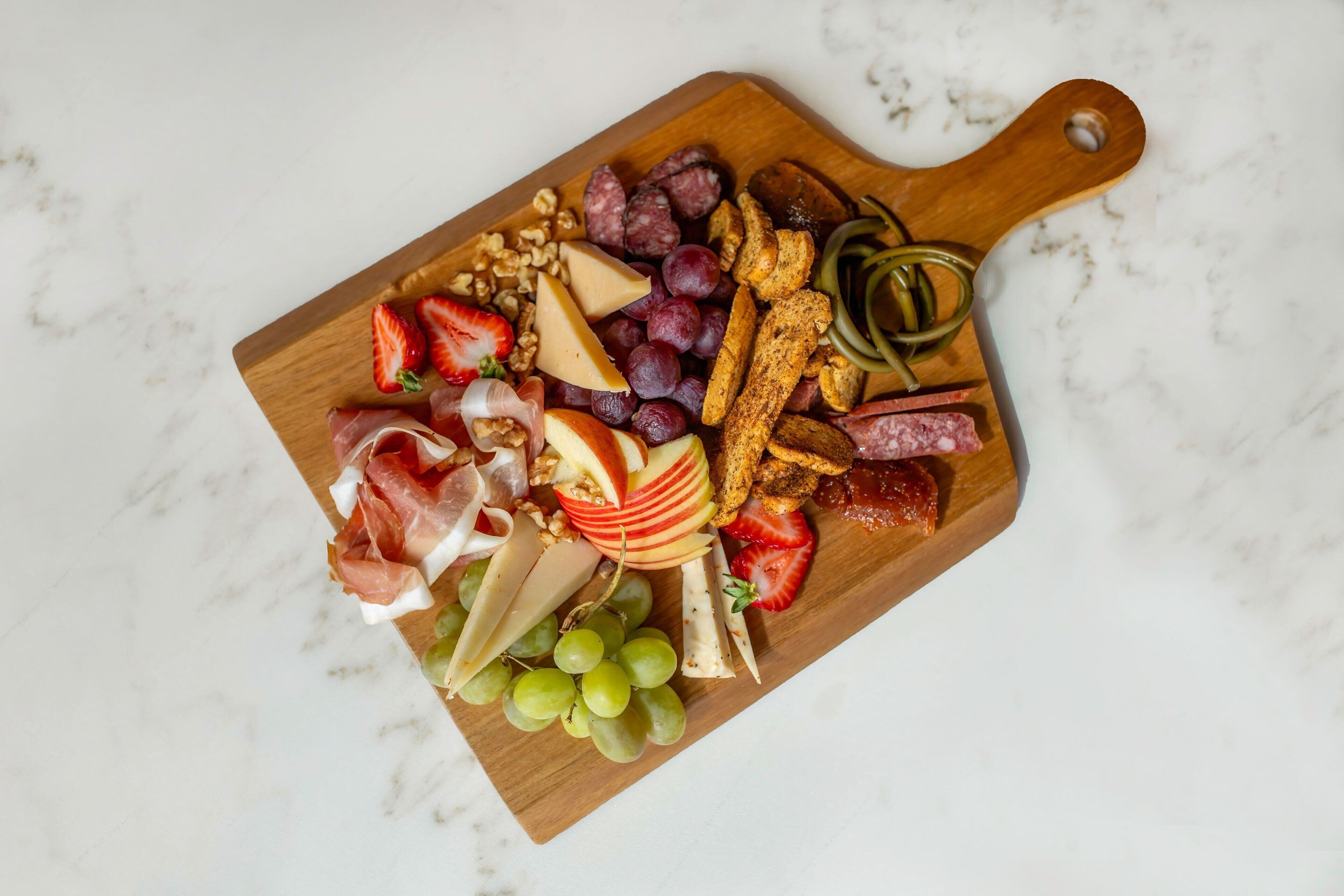 Una tabla de madera con varios quesos, frutas y aperitivos.