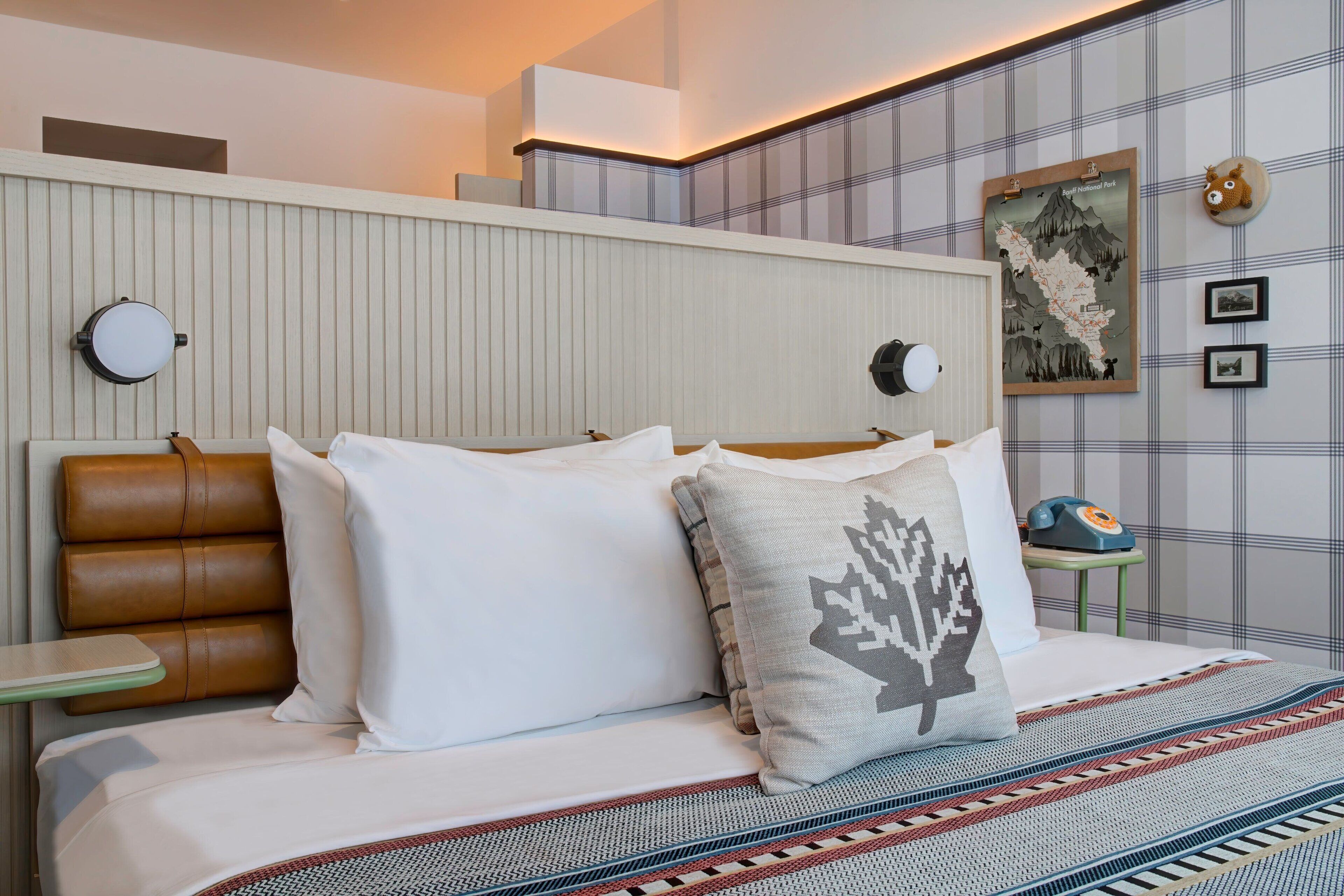 A hotel room with a bed, pillows, a headboard, a bedside table, a wall-mounted telephone, and a framed map.