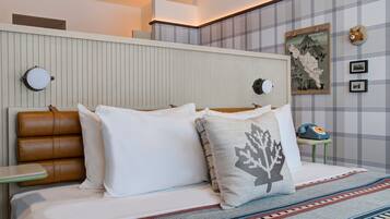 A hotel room with a bed, pillows, a headboard, a bedside table, a wall-mounted telephone, and a framed map.