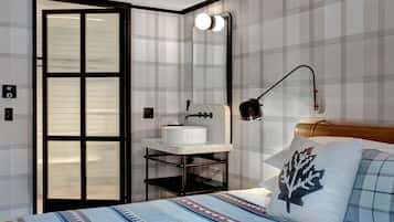 Un dormitorio con cama, mesita de noche con lámpara, lavamanos empotrado en la pared y puerta con paneles de vidrio esmerilado.