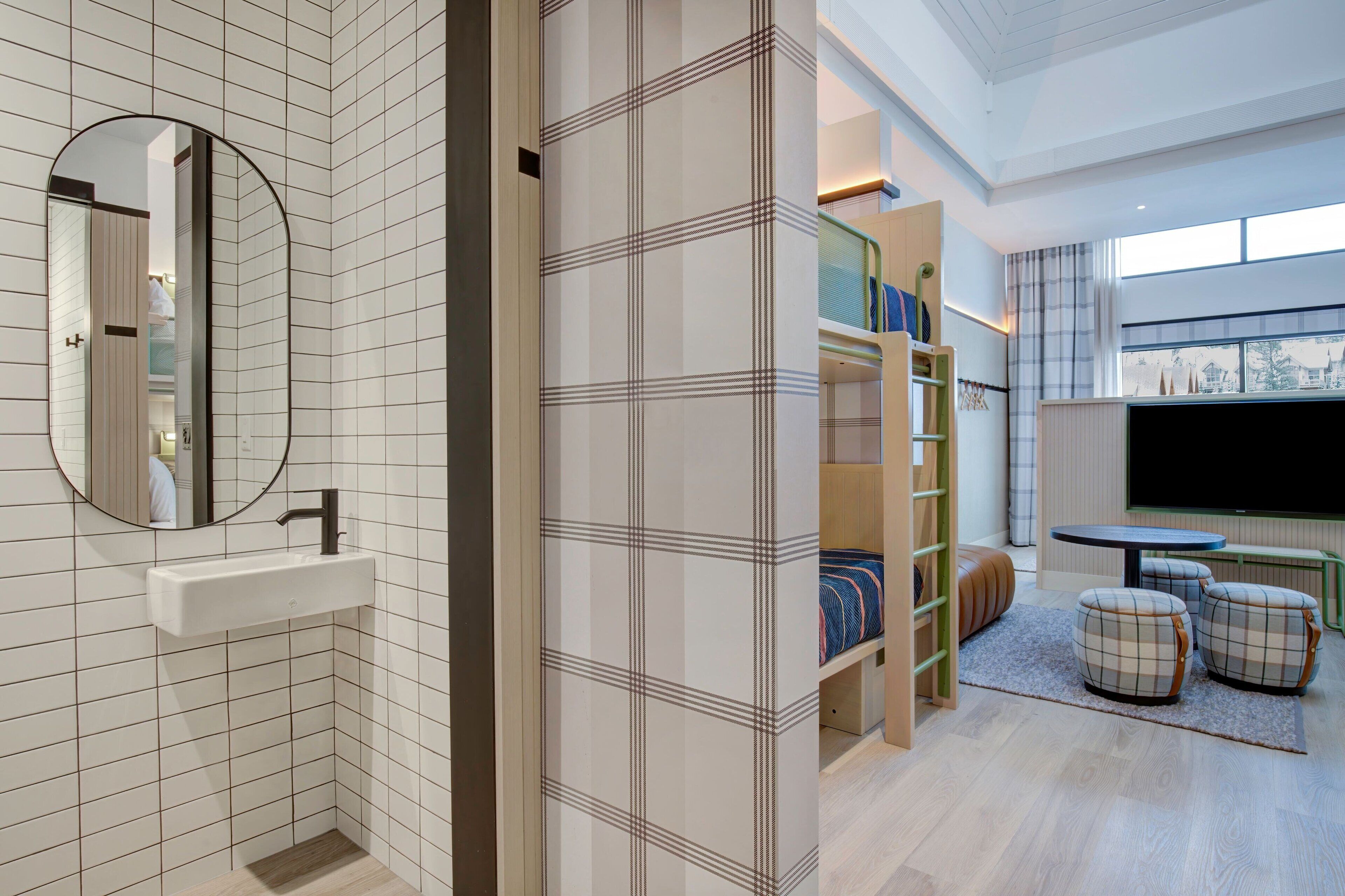 Un baño moderno con espejo, lavamanos y vistas a una sala de estar con televisión y asientos.