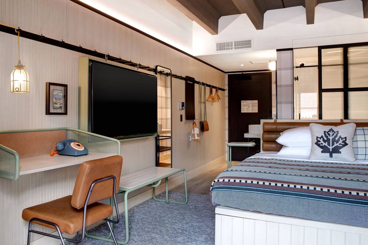 A modern hotel room with a large bed, a desk with a chair, a television, and a window with blinds.