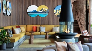 Een moderne woonkamer met een gele bank, houten bijzettafeltjes en een centraal haardelement.