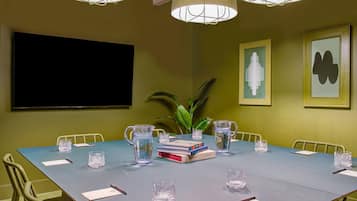 Un salón de conferencias con una larga mesa, sillas, una pantalla de proyector y obras de arte enmarcadas en las paredes.