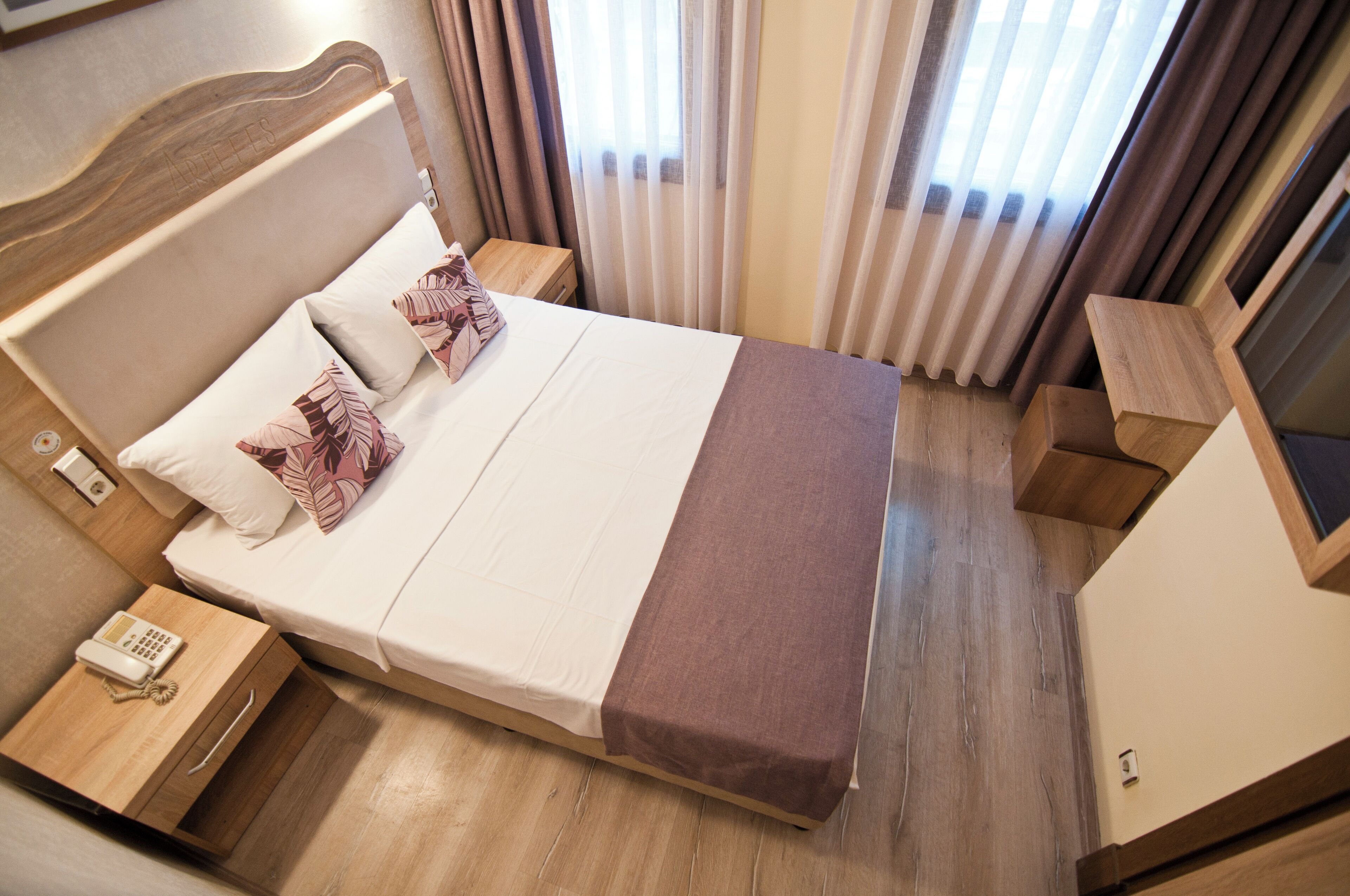 Una camera d'albergo con un letto, comodini, un telefono e tende.