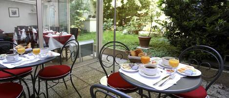 Un café al aire libre con mesas y sillas, comida para el desayuno y vistas a un jardín.