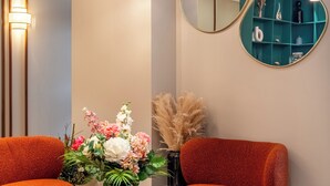 Una sala moderna con una mesa redonda de madera, dos sillones naranja, un jarrón con flores y dos lámparas colgantes.