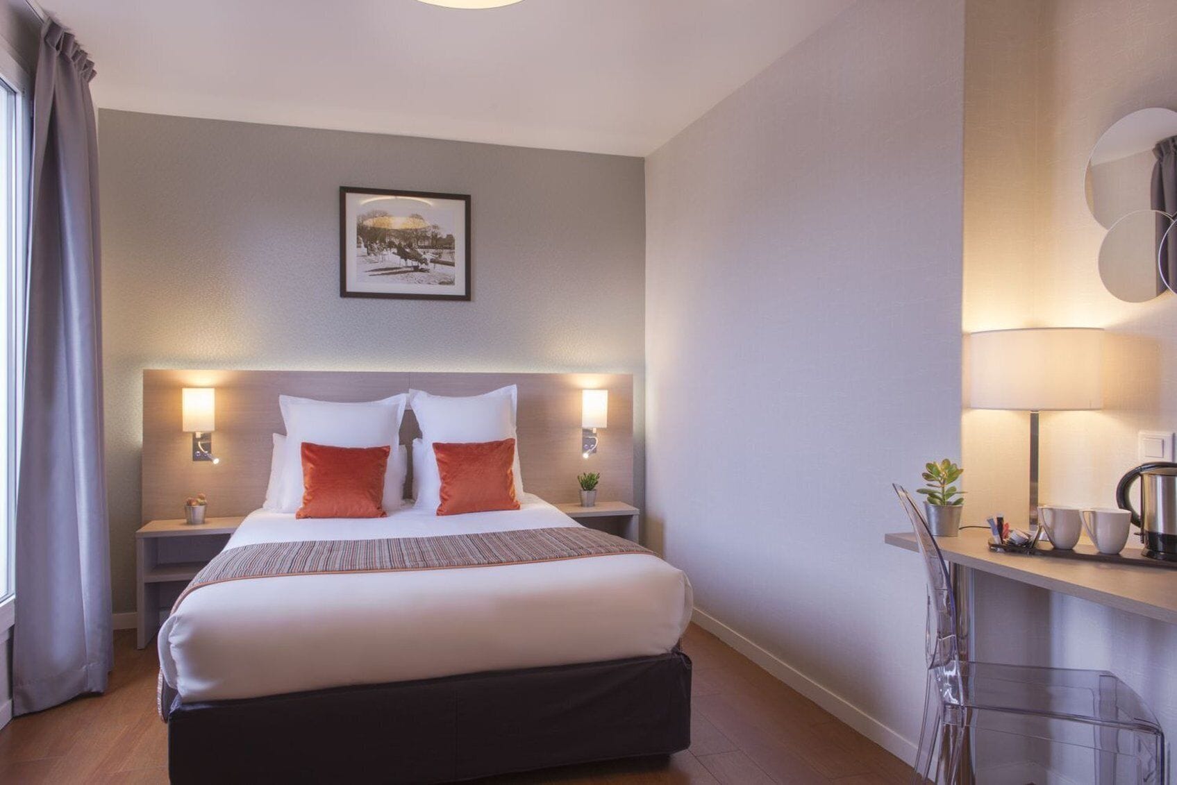 A hotel room with a large bed, bedside tables, a desk with a lamp, and a picture on the wall.