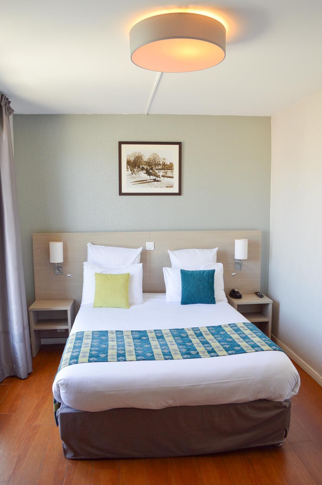 Hotelkamer met een groot bed, twee nachtkastjes, een lampje en een schilderij aan de muur.