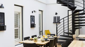 Un espace repas moderne avec une table en bois, des chaises noires et un escalier en colimaçon noir.