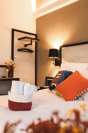 Quarto de hotel moderno com cama, mesas de cabeceira, luminária na parede e um vaso decorativo com flores.
