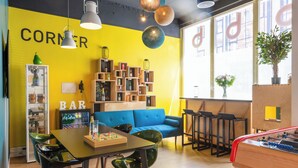 A vibrant room with a yellow wall, a blue sofa, a wooden table with chairs, a bookshelf, and a foosball table. - Hôtel Bootcamp (Issy-les-Moulineaux)