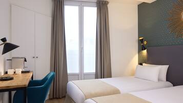 Ein Hotelzimmer mit zwei Betten, einem Schreibtisch mit Stuhl, einer Lampe und einem Fenster mit Vorhängen.
