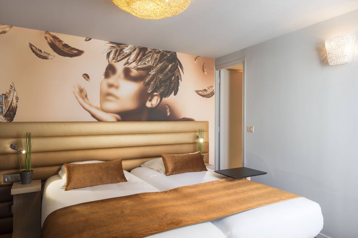 Une chambre d’hôtel moderne avec un grand lit, une tête de lit ornée de lignes horizontales, une œuvre d’art accrochée au mur et une petite table sur laquelle est posée une plante.