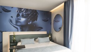 Una camera d'hotel moderna con un letto grande, un comodino, uno specchio a parete e un murale decorativo.