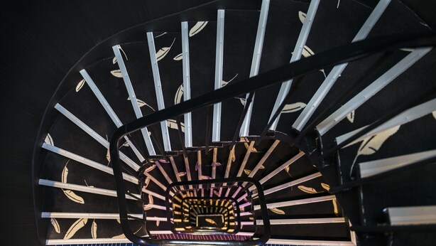 Una scala a chiocciola con una piattaforma panoramica centrale, circondata da ringhiere in metallo e piastrelle decorative.
