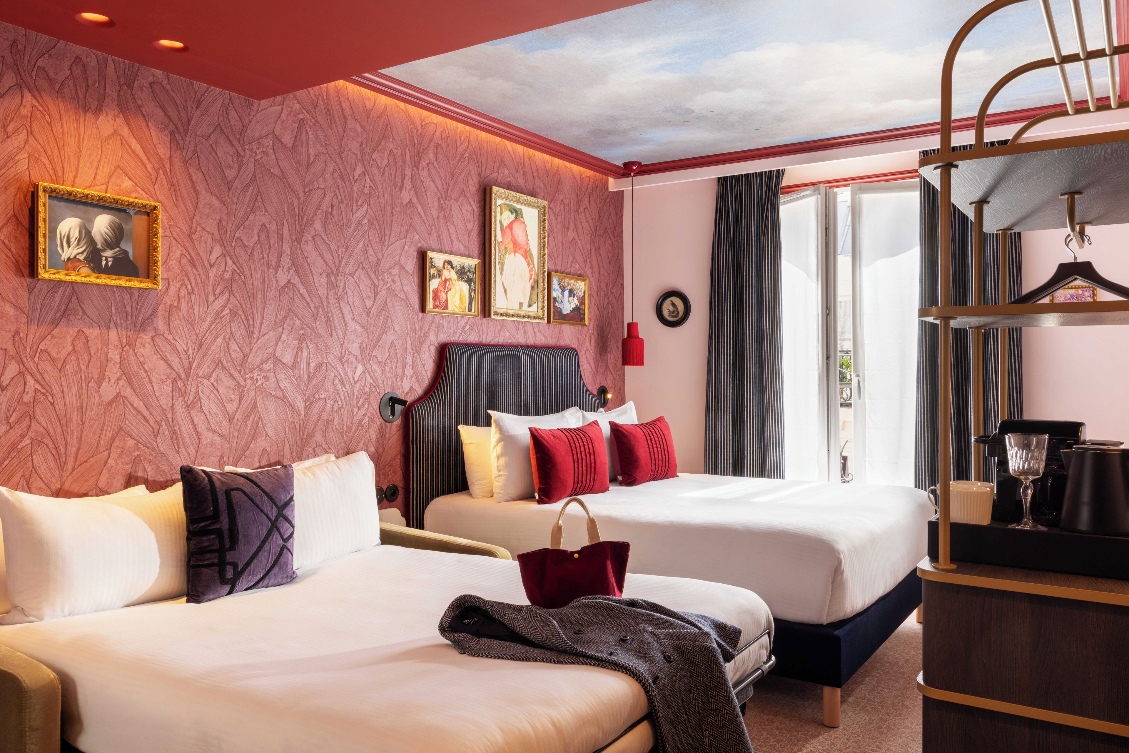 Habitació d'hotel amb dos llits, una finestra gran i vista al cel.
