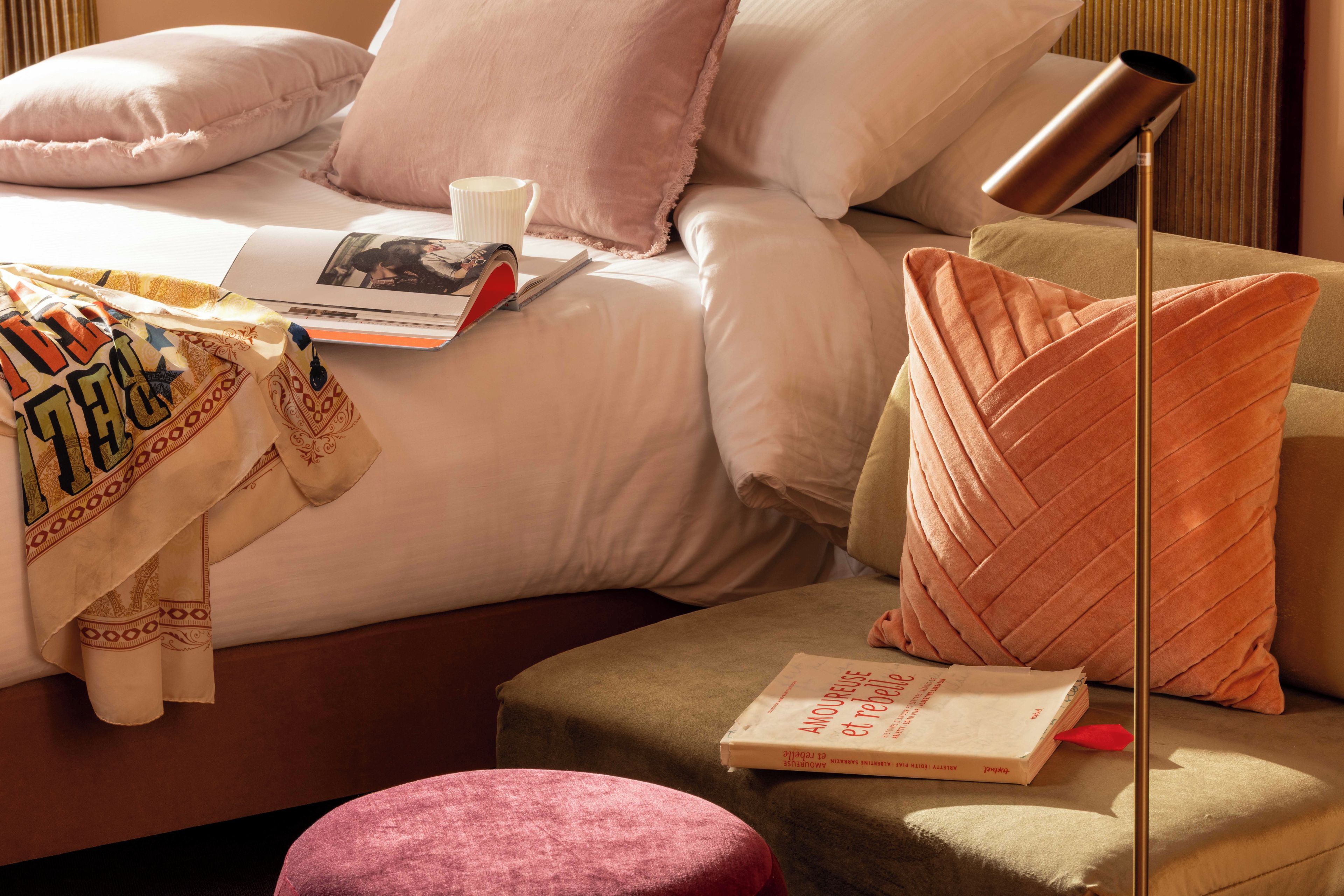 Un dormitorio ordenado con cama, almohadas, una mesita de noche, una lámpara y un libro.
