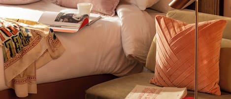 Une chambre à coucher bien rangée, avec un lit, des oreillers, une table de chevet, une lampe et un livre.