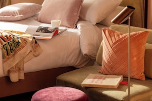 Una camera da letto ordinata con un letto, cuscini, un comodino, una lampada e un libro.
