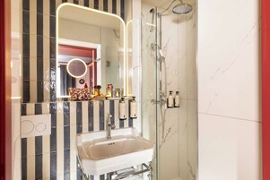 A bathroom with a white sink, a glass shower enclosure, and a mirror with a circular light.