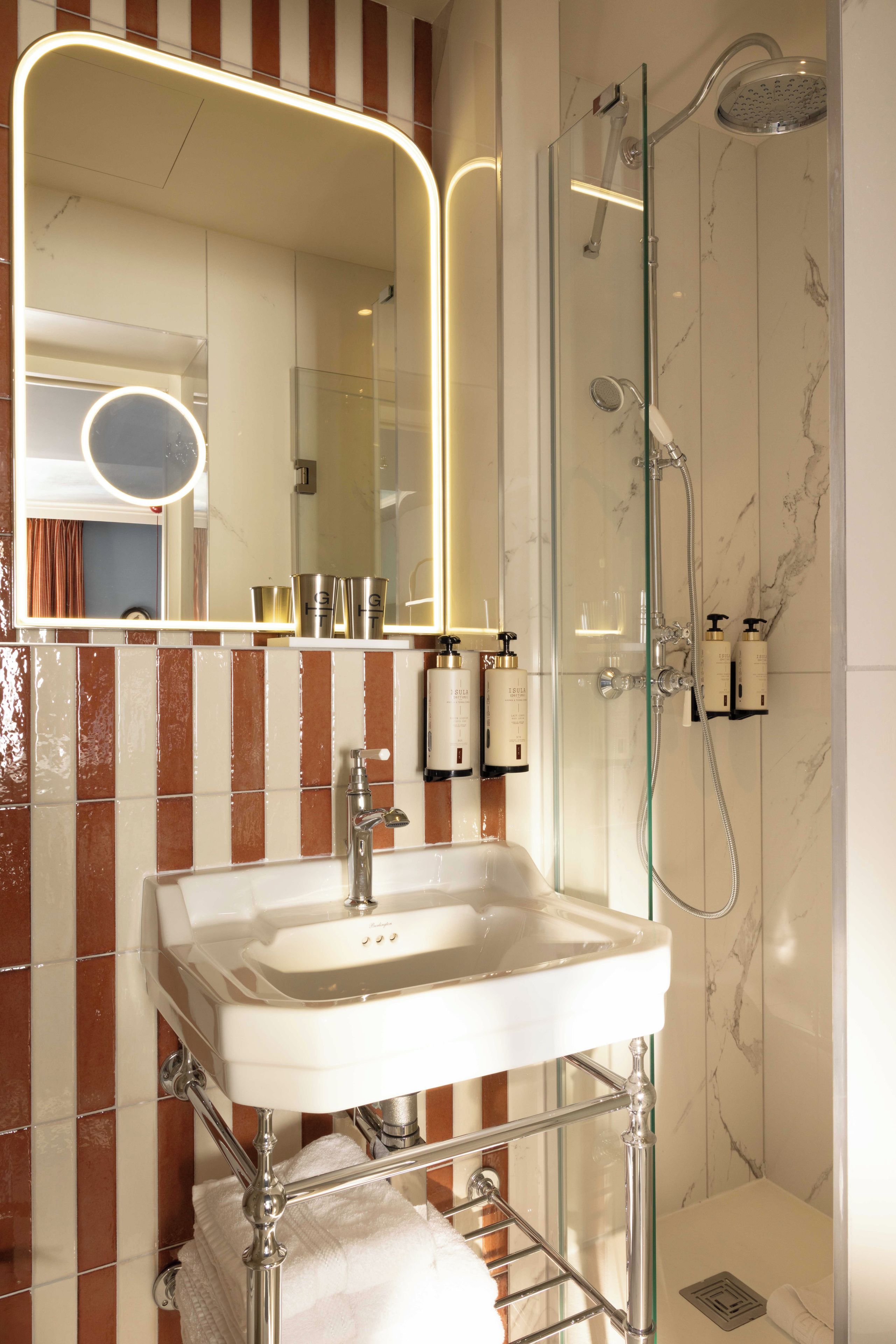 Une salle de bain avec une douche à parois de verre, un lavabo blanc et un miroir doté d’un cadre éclairé.