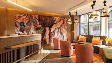 Un espace d’accueil moderne avec un comptoir en bois, une fresque murale, des sièges avec des coussins orange et une vue sur la rue grâce à de grandes fenêtres.