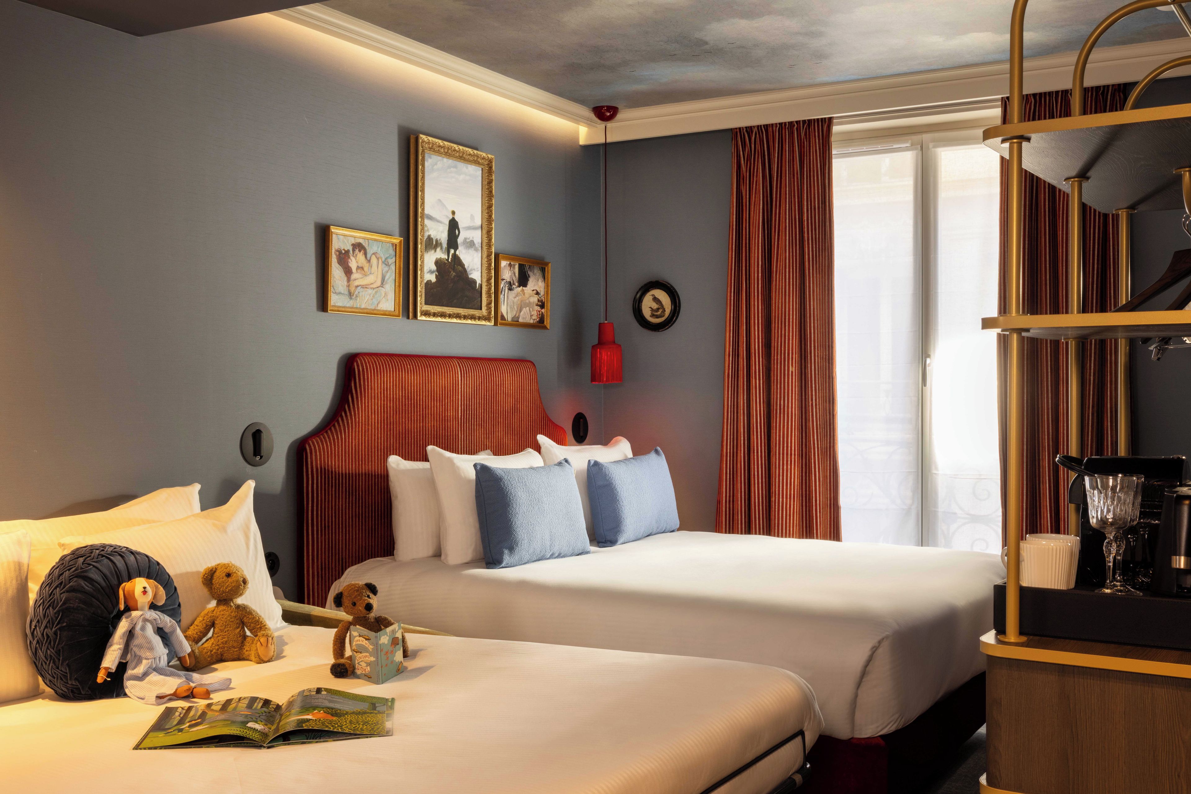 Habitación de hotel con dos camas, una estantería, un ventanal con cortinas y decoración en la pared.