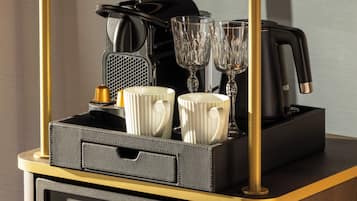 Una cafetera negra y dorada con dos tazas blancas y dos vasos de cristal sobre una bandeja.