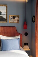 Un dormitorio con una cama, dos obras de arte enmarcadas, una lámpara colgante roja y una mesita de noche con dos objetos negros.