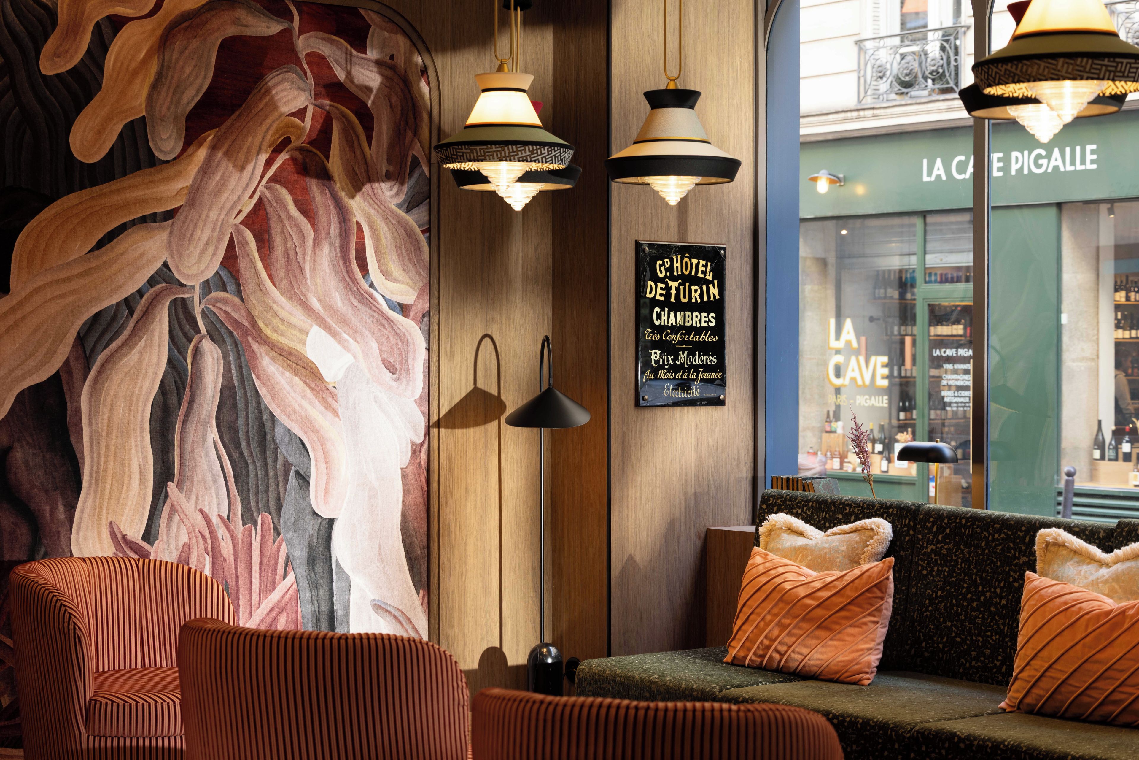 Un vestíbulo de hotel con un cuadro abstracto de grandes dimensiones, una pared de madera, un sofá con cojines naranjas y un cartel que dice 'G.P. HOTEL DE TURIN CHAMBRES'.