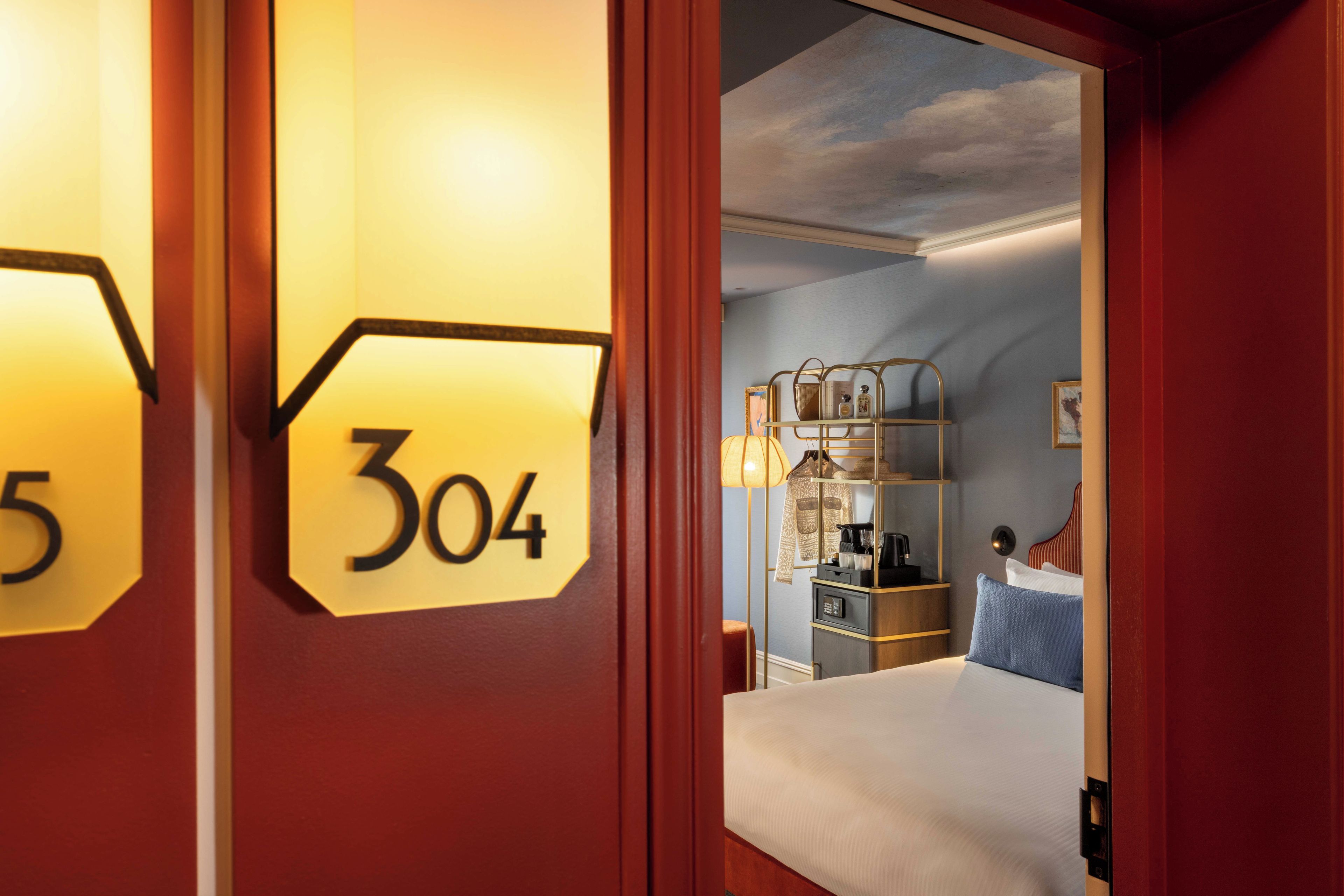 Una camera d'hotel con un letto, un comodino, una lampada e uno scaffale con diversi oggetti.