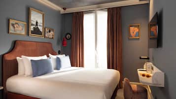 Una camera d'albergo con un letto grande, una scrivania con una lampada e opere d'arte alle pareti.