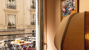 Una habitación con vista a la calle, una mesa con un sombrero y gafas, y un cuadro en la pared.