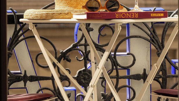 A balcony with a metal railing, a wicker hat, a wine glass, and a book titled 'RENÉ'.