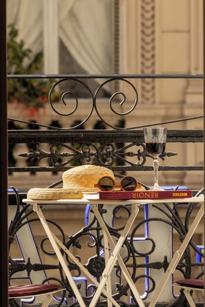 A balcony with a metal railing, a wicker hat, a wine glass, and a book titled 'RENÉ'. - Grand Hotel De Turin (Paris)