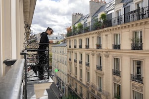 A balcony with wrought iron railings overlooking a narrow street with buildings.