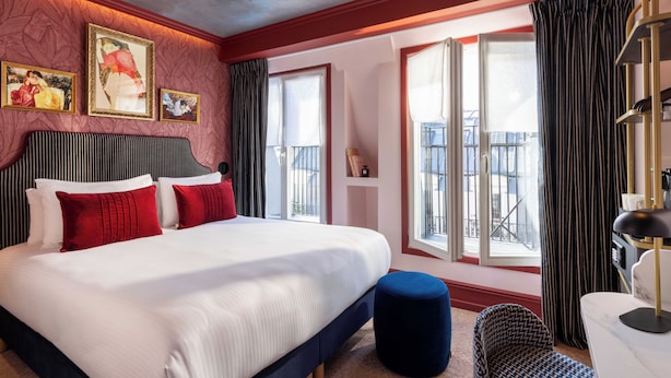 Una habitación de hotel con una cama grande, un balcón con cortinas y una obra de arte en la pared.