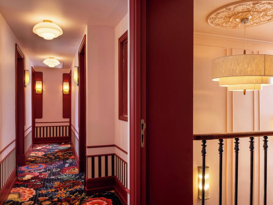A hotel hallway with a carpeted floor, wooden doors, and wall-mounted light fixtures.