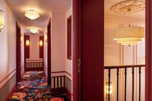 A hotel hallway with a carpeted floor, wooden doors, and wall-mounted light fixtures. - Grand Hotel De Turin (Paris)