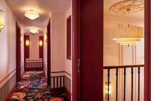 Un corridoio d'albergo con pavimento rivestito di moquette, porte in legno e lampade fissate al muro.