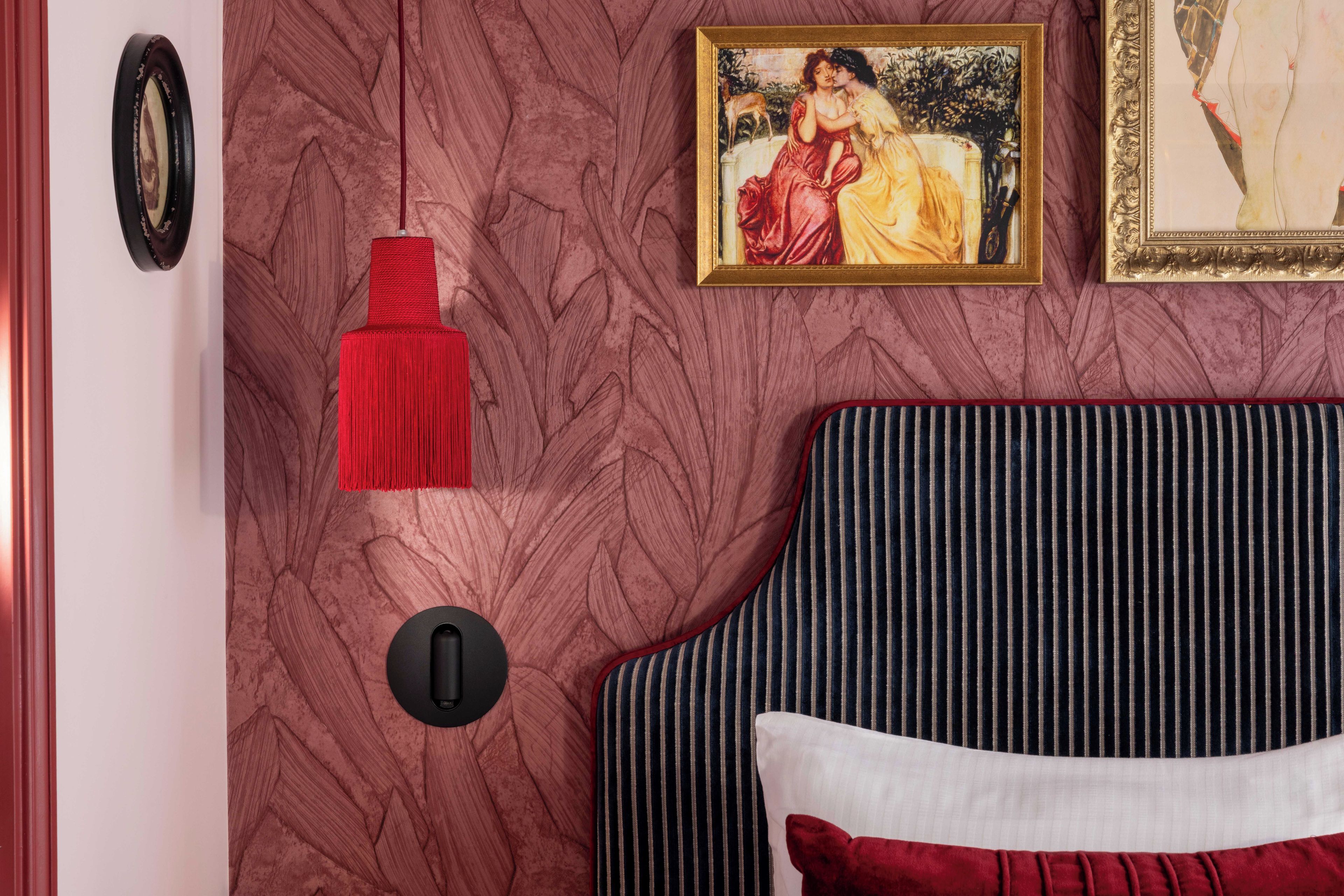 Une pièce avec un lit, une houppe rouge suspendue au plafond, un tableau encadré au mur et une porte dotée d’une poignée ronde.