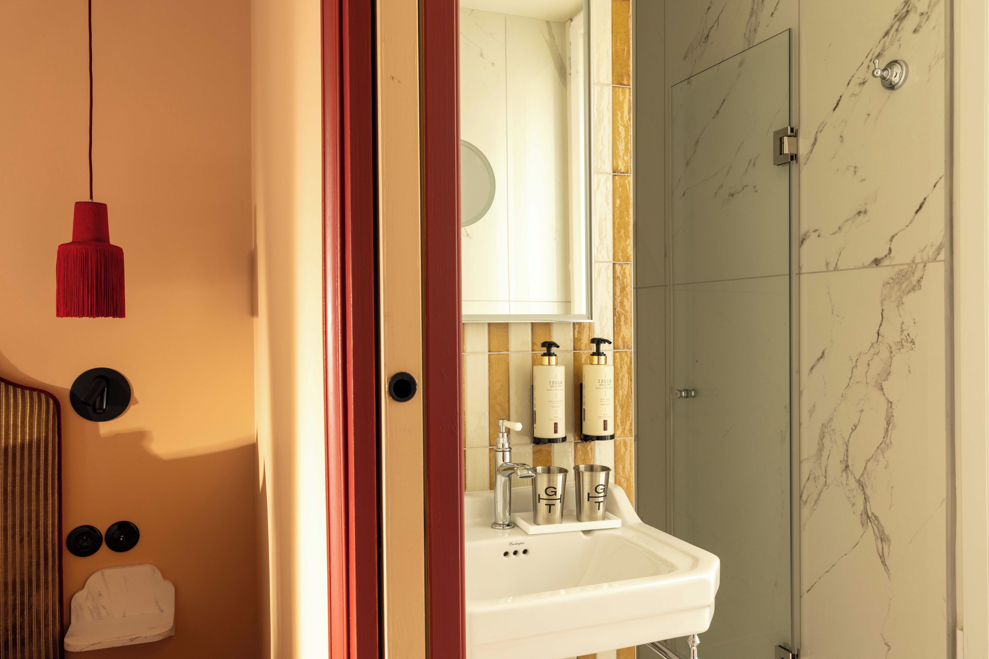 A bathroom with a white sink, two bottles of shampoo, a mirror, and a shower with marble tiles.