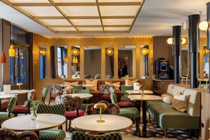 Un hall d’hôtel avec des tables rondes, des chaises à motifs, un canapé et une machine à café.