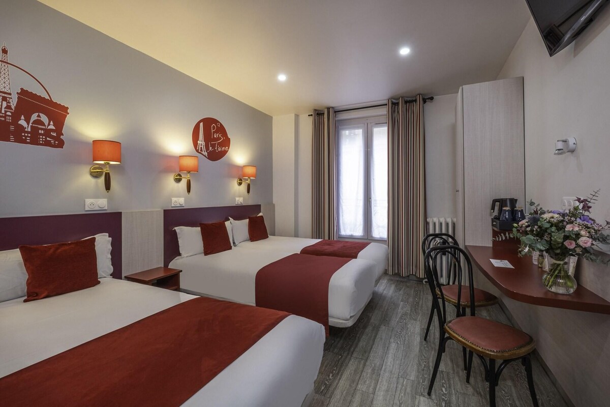 A hotel room with two beds, a desk with a chair, a vase of flowers, and a view of the Eiffel Tower.