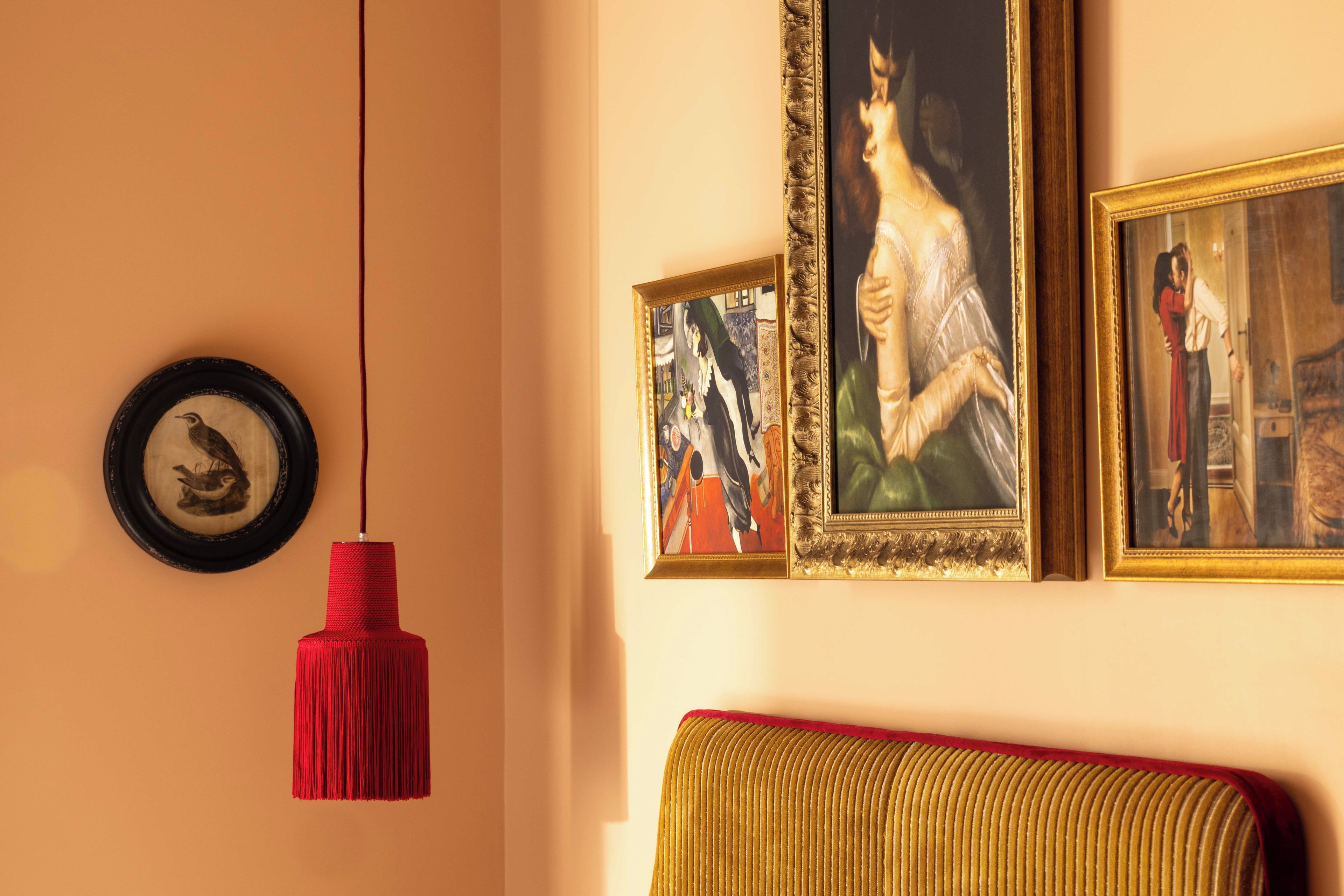 Une pièce avec un luminaire suspendu rouge, un tableau encadré représentant un oiseau et un canapé agrémenté d’un coussin rouge.