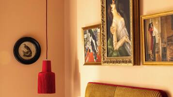 Une pièce avec un luminaire suspendu rouge, un tableau encadré représentant un oiseau et un canapé agrémenté d’un coussin rouge.