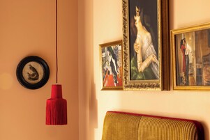 A room with a red pendant light, a framed picture of a bird, and a sofa with a red cushion.