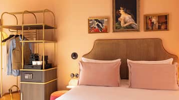 Een hotelkamer met een bed, een kledingkast met daarin hangende kleding, een koffiezetapparaat en een tafeltje met een lamp.